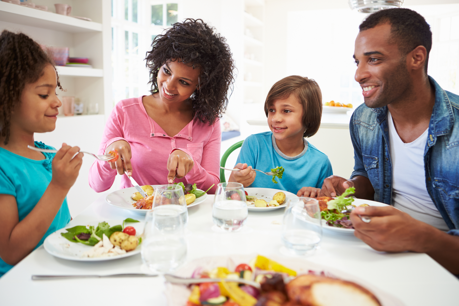 Na tym ujmującym obrazku widzimy rodzinę, która siedzi razem przy białym stole i cieszy się wspólnym posiłkiem. Atmosfera jest spokojna i pełna harmonii, a obraz oddaje ważność jedzenia w towarzystwie najbliższych. Rodzina jest skupiona wokół stołu, który jest pokryty białym obrusem. Widzimy rodziców i dzieci, którzy mają na talerzach ułożone jedzenie. Ich twarze są pełne uśmiechu i radości, co świadczy o tym, że są szczęśliwi i zadowoleni z obecności siebie nawzajem